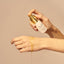 Hand applying a Pigmentation Oil product from 'The Face Company' to a wrist against a beige background