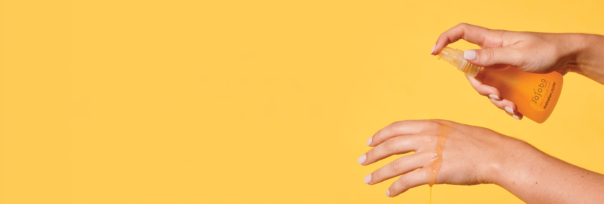 Hands dispensing clear liquid from a bottle onto another hand against a yellow background.