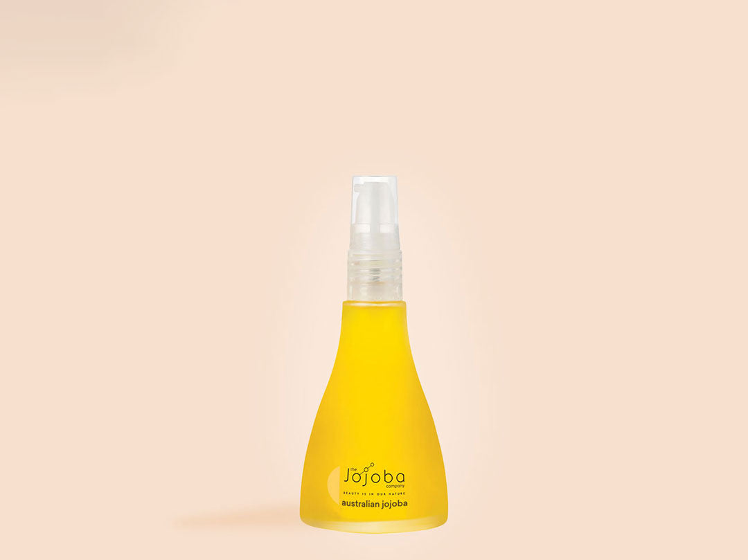 Yellow jojoba oil spray bottle on a pale background.