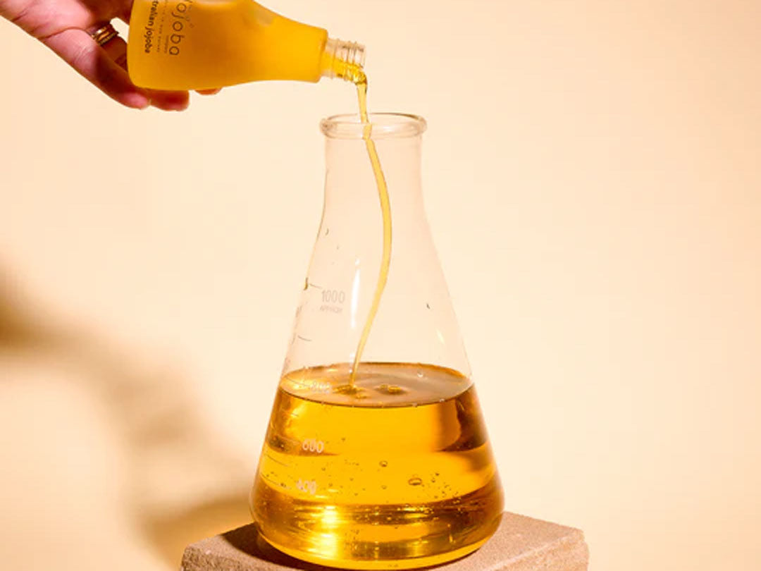 Liquid being poured into a flask from a bottle against a beige background.