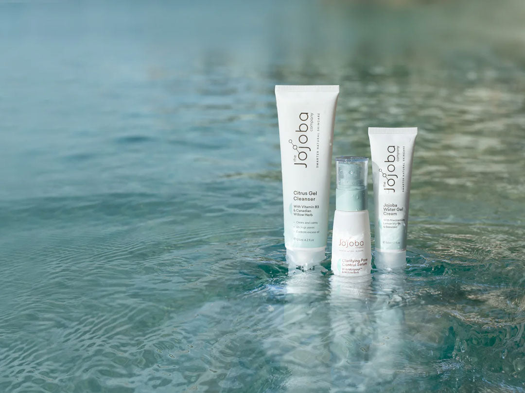 Skincare products by Jojoba displayed in shallow water with light ripples.