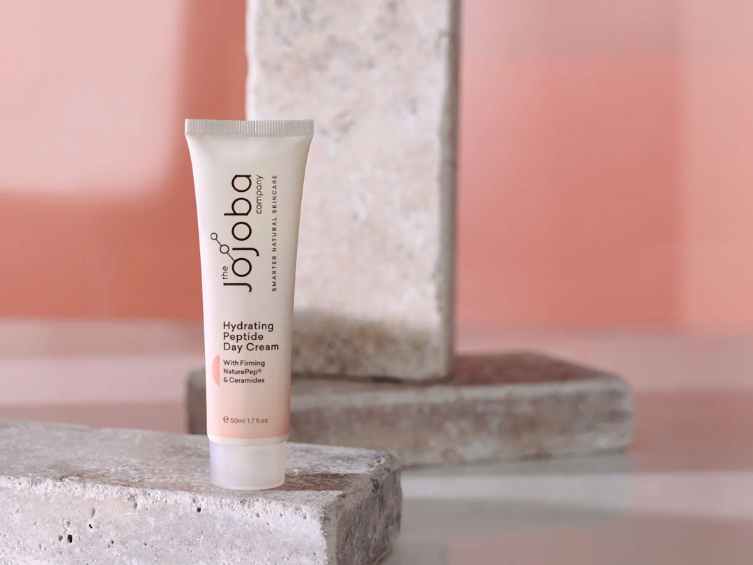 Tube of hydrating peptide day cream on a stone surface with a soft pink background.