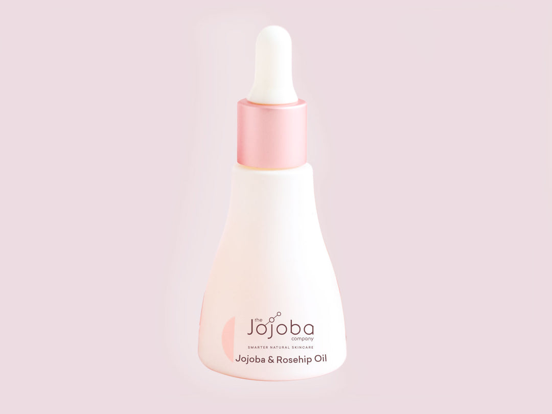 Bottle of Jojoba & Rosehip Oil by The Jojoba Company on a pink background.