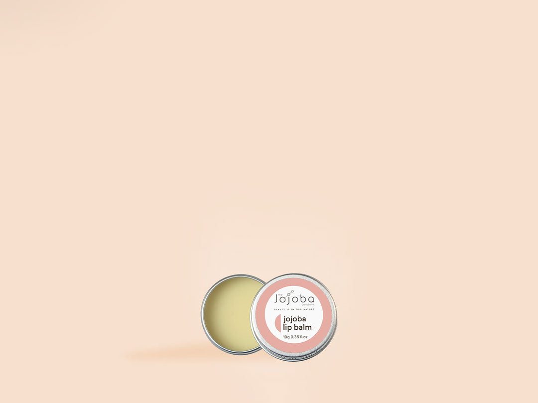 Open tin of jojoba lip balm on a beige background.