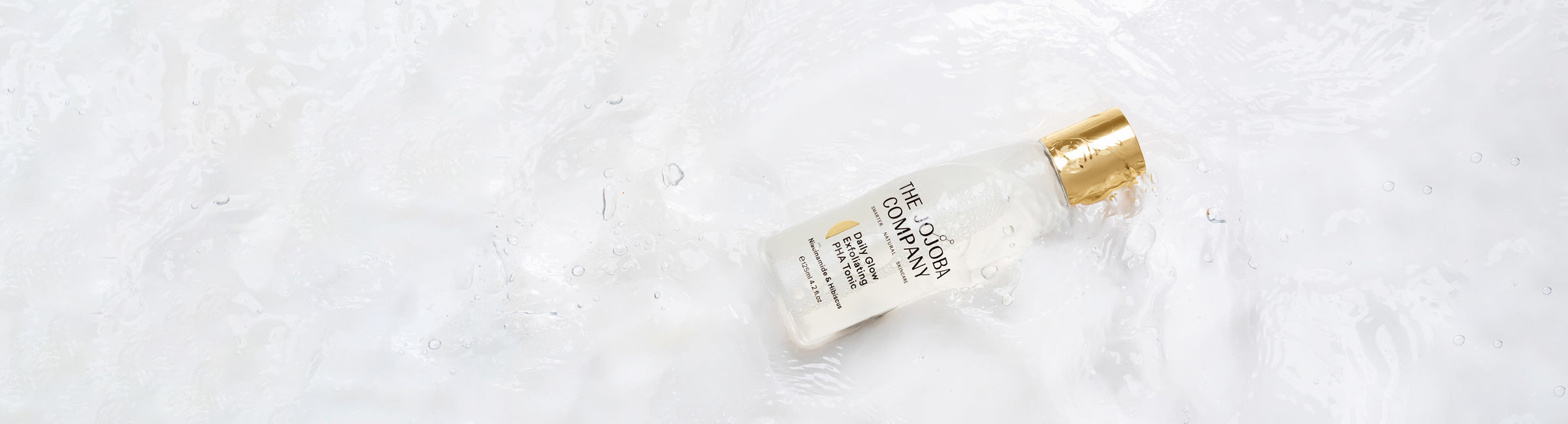 A bottle of The Jojoba Company skincare product lying on a wet surface.