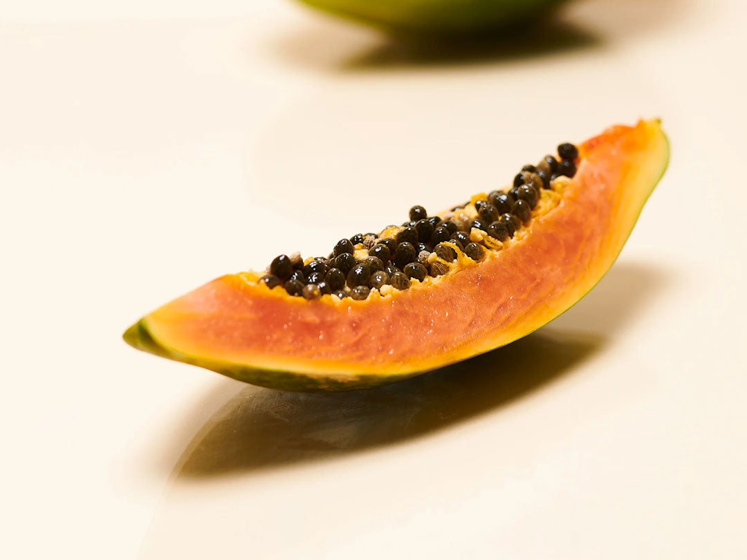 Slice of ripe papaya with black seeds on a white background.