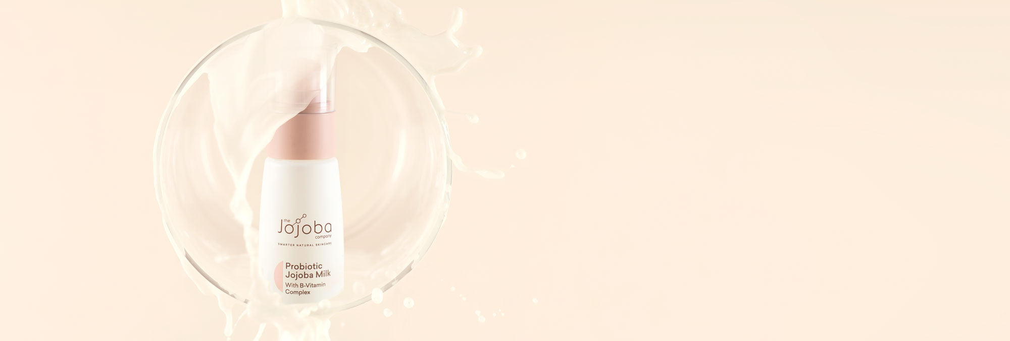 A bottle of Probiotic Jojoba Milk skincare product with a splash effect on a soft peach background.