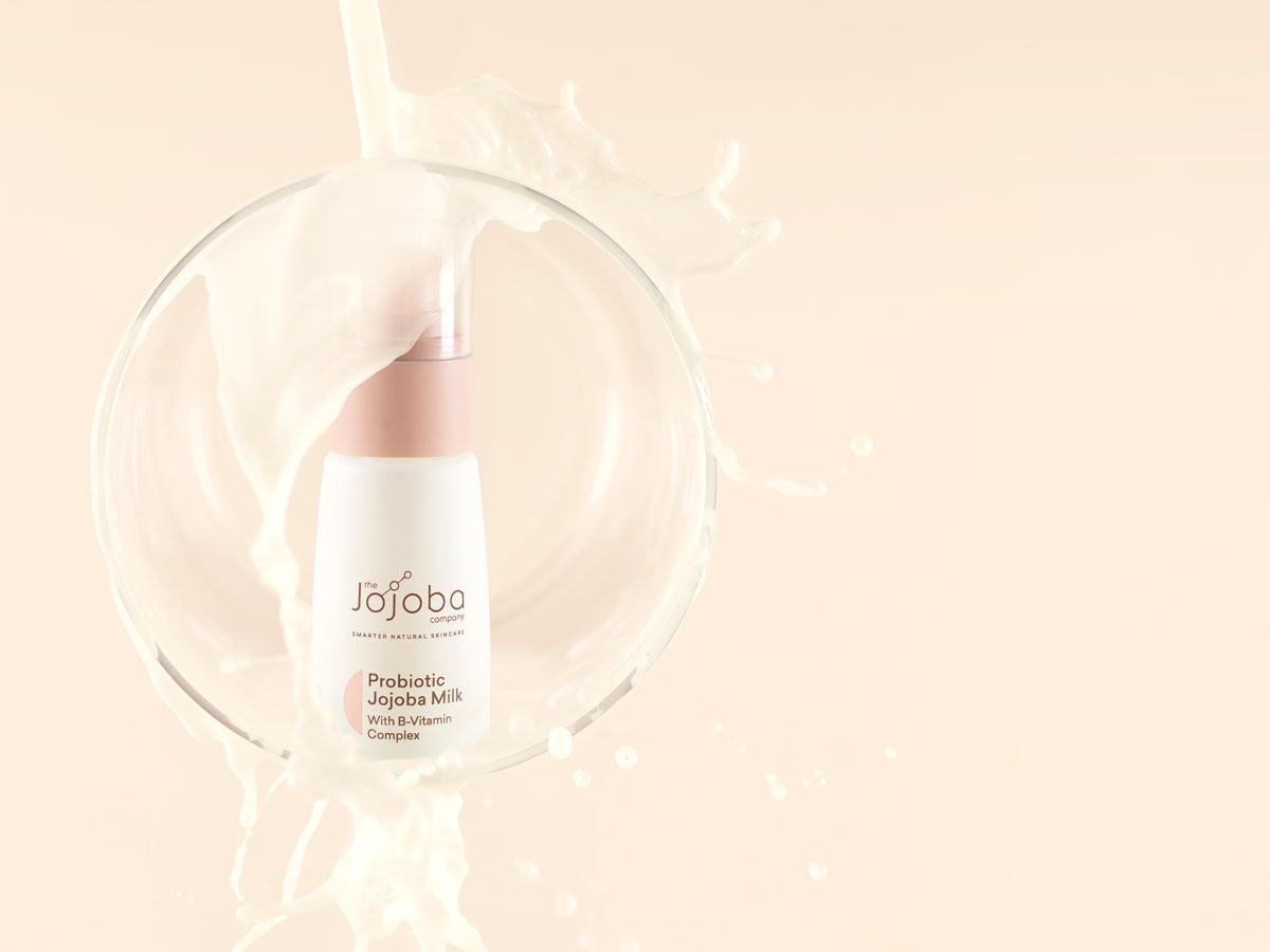 A bottle of Jojoba Milk skincare product with dynamic milk splash around it on a peach background.