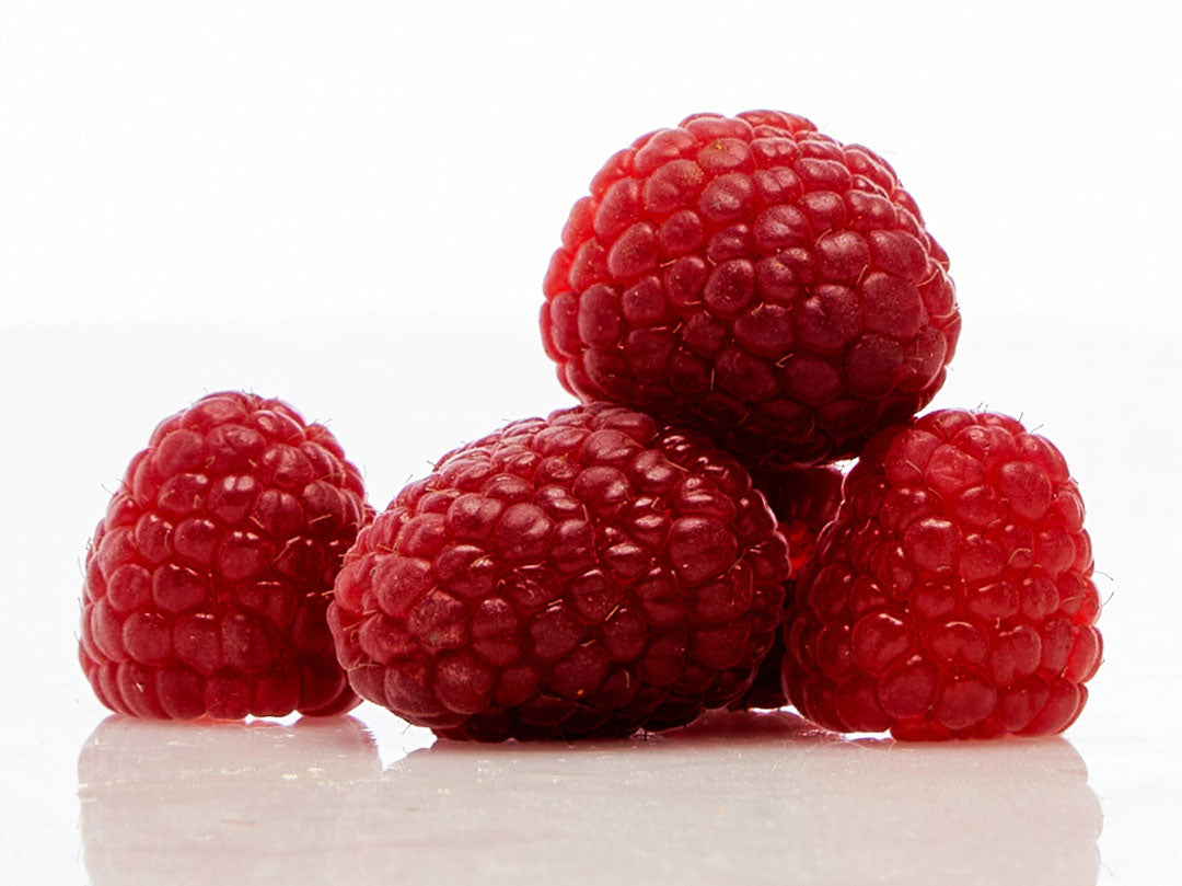 Five ripe raspberries stacked on a reflective white surface.