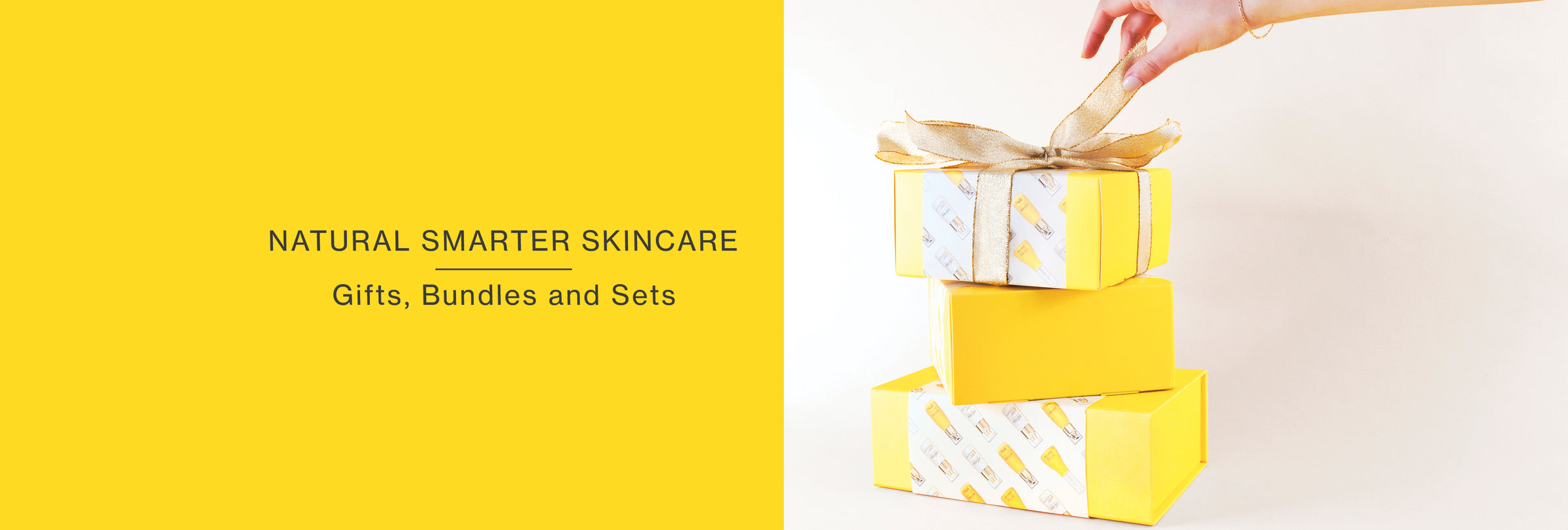 Hand tying bow on yellow skincare gift boxes with slogan 'NATURAL SMARTER SKINCARE Gifts, Bundles and Sets'.