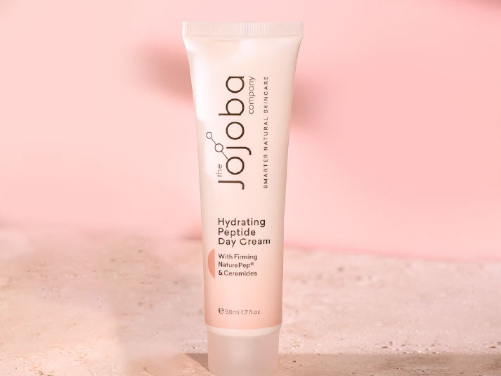 Tube of "The Jojoba Company Hydrating Peptide Day Cream" on a pink background.