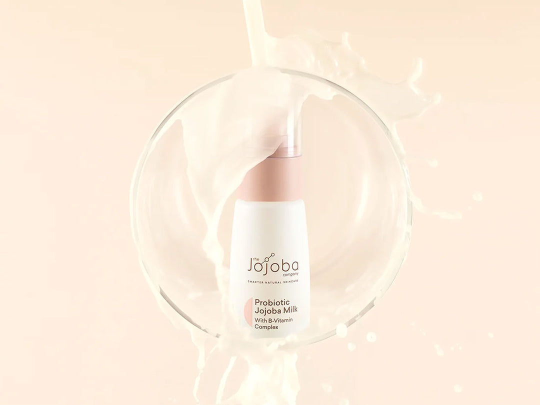 A bottle of Jojoba Milk with splashing liquid on a peach background.