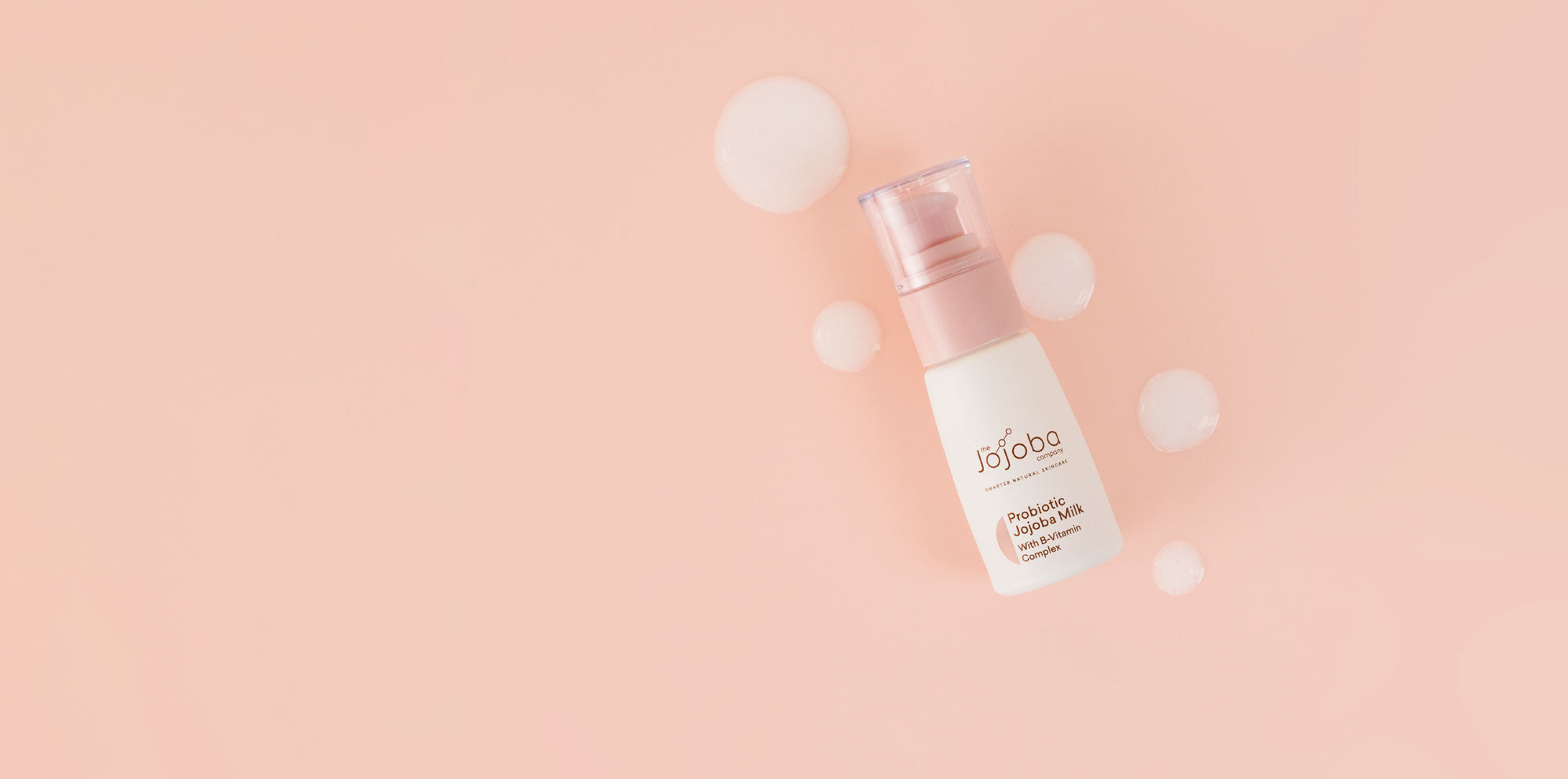 Skincare product bottle with probiotic label surrounded by white spheres on a pastel background.