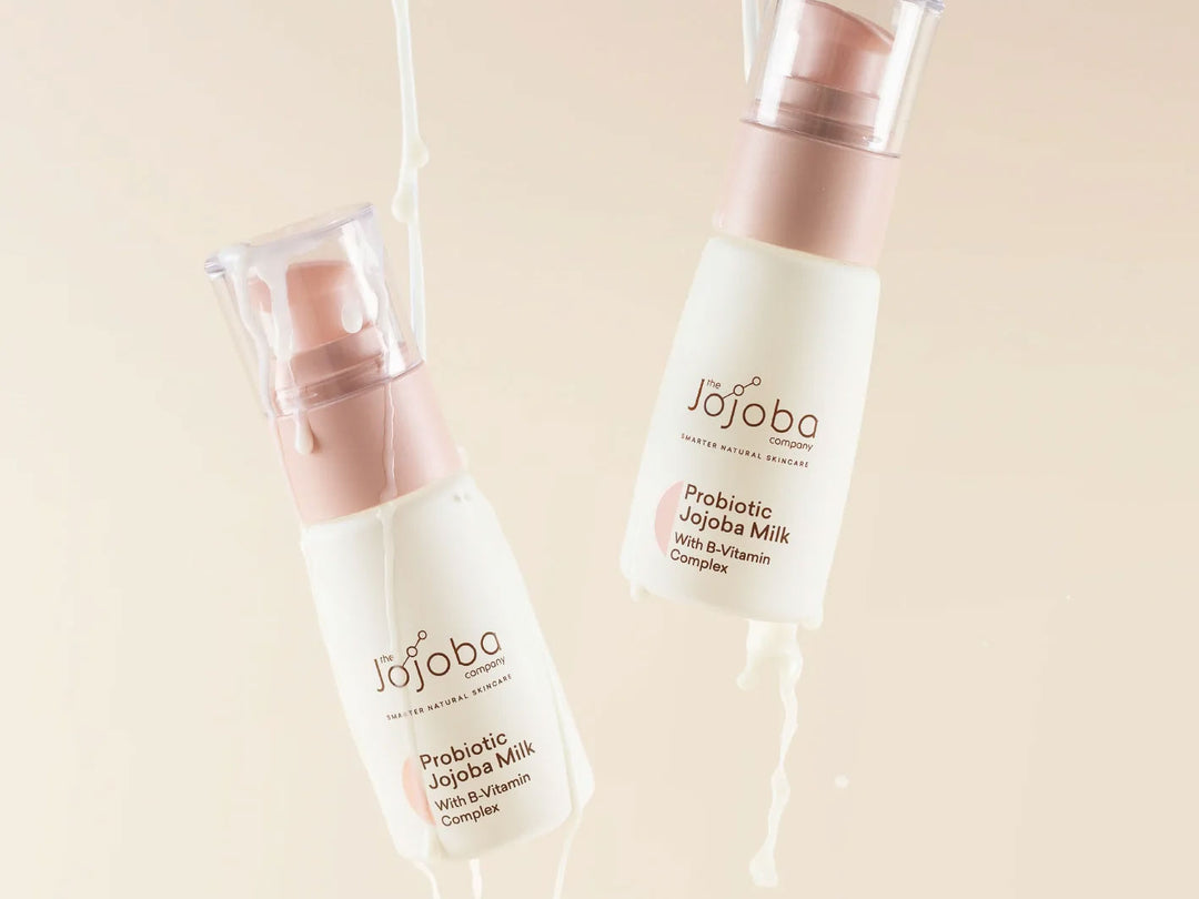 Two bottles of Jojoba probiotic skincare milk with product flowing out, against a beige backdrop.