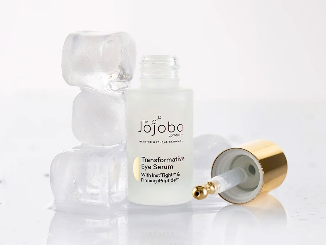 Eye serum bottle with pipette and ice cubes on a reflective surface.