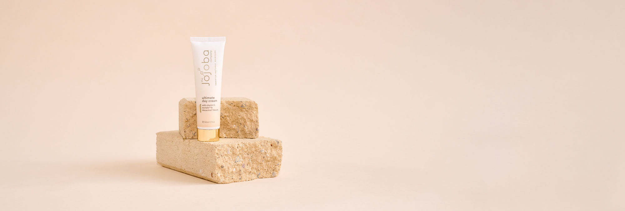 Skincare cream tube on stone blocks against a beige background.