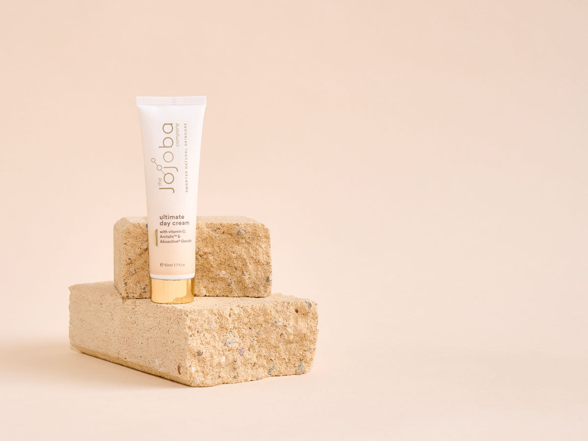 Tube of jojoba day cream on a cork block against a beige background.