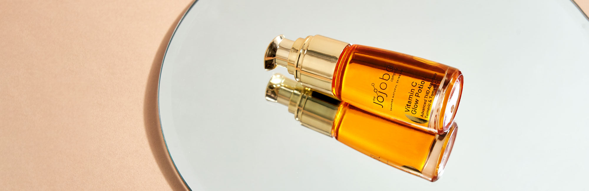 Two amber-colored facial serum bottles on a reflective surface with golden caps.