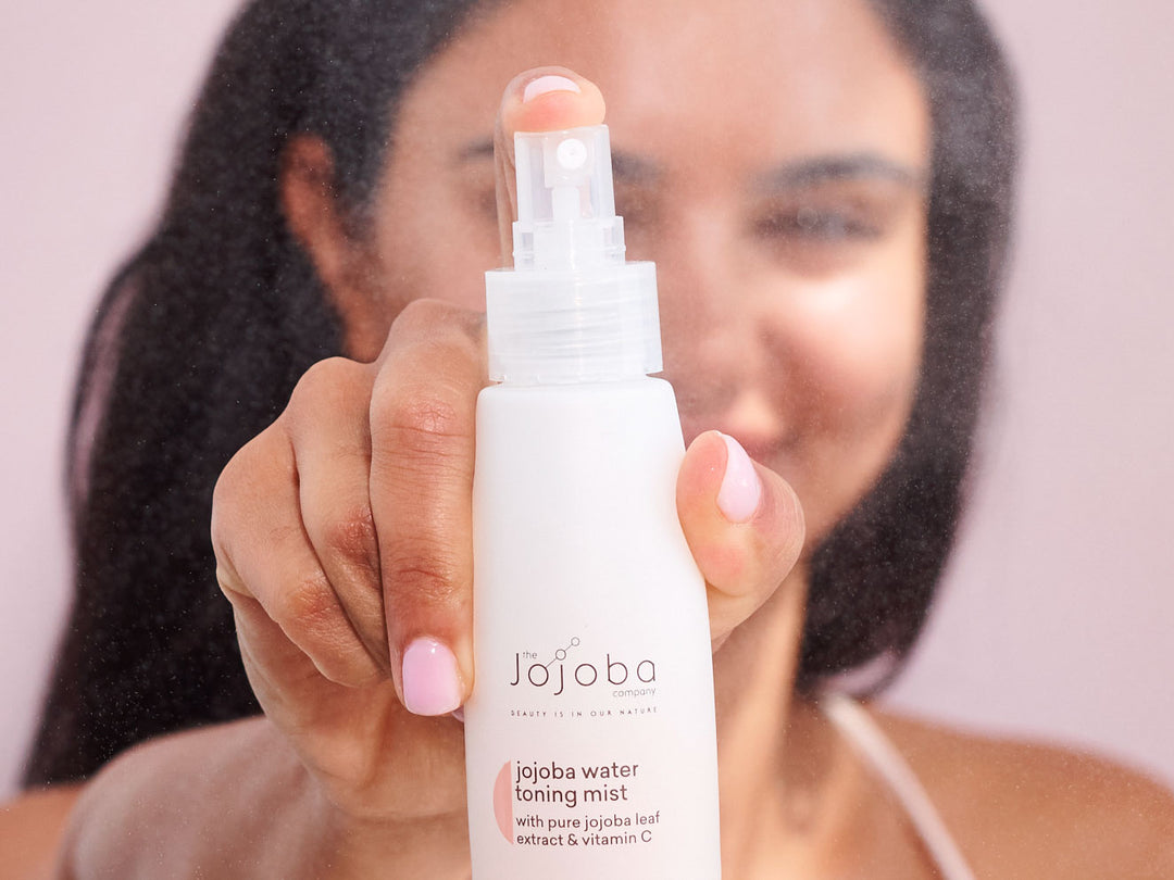 A person holding a jojoba toning mist bottle, with focus on the product.