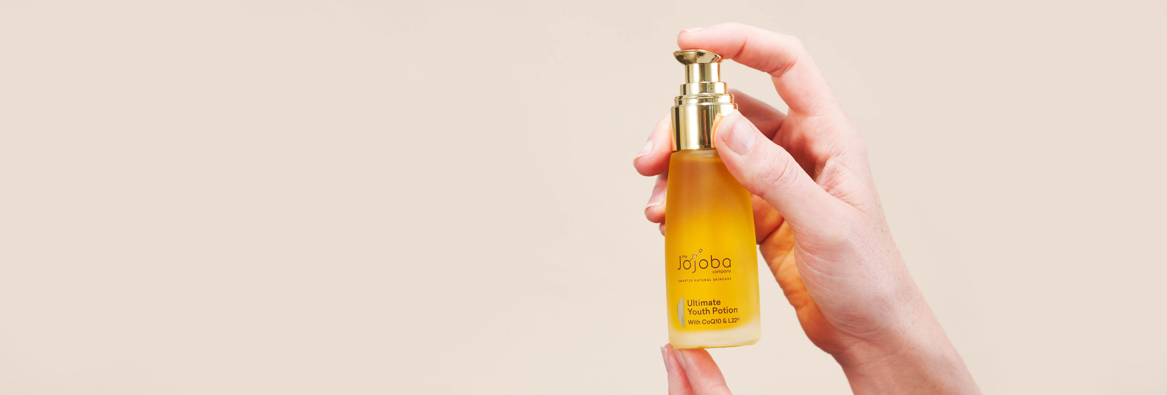 Hand holding a bottle of Jojoba Company Ultimate Youth Potion against a pale background.