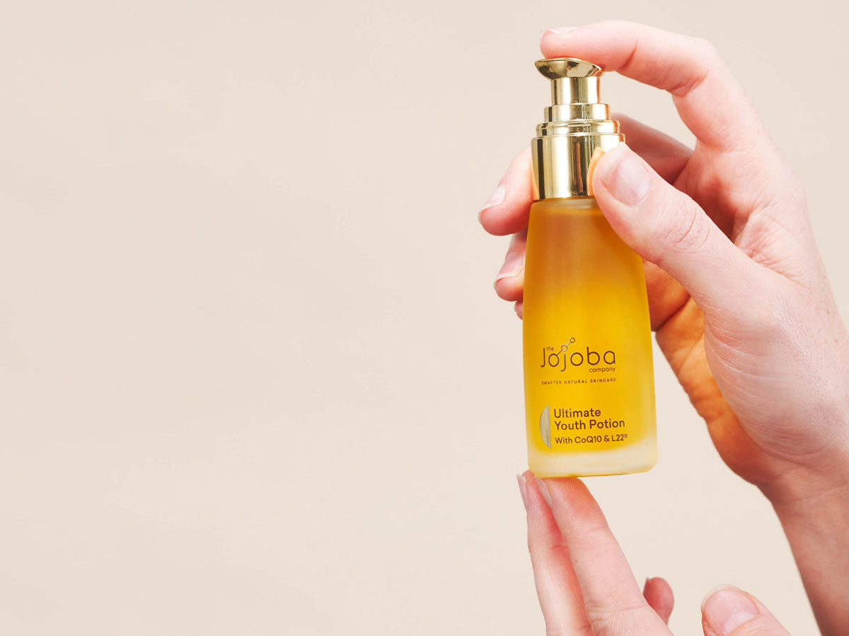 Hands holding a bottle of Jojoba Ultimate Youth Potion skincare product.